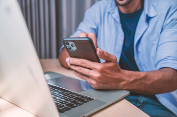 A man sitting in home and using mobile phone and laptop computer. 