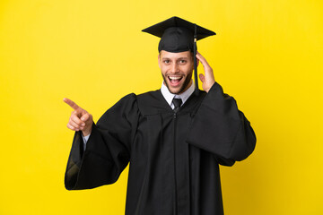 Young university graduate caucasian man isolated on yellow background surprised and pointing finger to the side