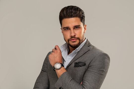 Fashion portrait of handsome elegant businessman with beard, wearing luxury handwatch, looking at the camera.