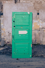 Detached green door with damaged stone house wall on the background. Old, weathered wooden door on construction site with empty white arrow sign. Abandoned building reconstruction. Moody, creative
