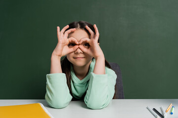 Preteen schoolkid gesturing near notebook and chalkboard at background.
