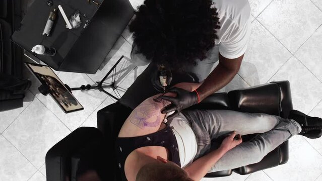 Tattoo master makes a tattoo on a man body. View from above. High quality 4k footage