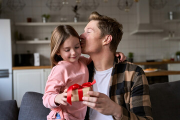 Happy cute child daughter embracing dad making present at home on Fathers Day. Smiling family young...