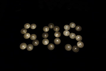 sos save our souls written with burning candles isolated on black background
