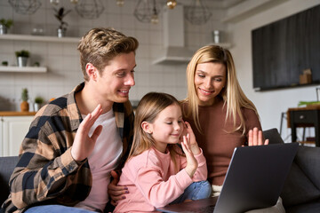 Happy young family parents with child kid daughter waving hands, talking, video calling using laptop computer at home having virtual meeting in online webcam chat videocall together sitting on sofa.