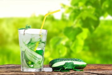 Refreshing drink with cucumber and mint, in a glass with a straw, next to ice cubes, against a...