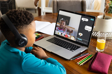 Biracial boy wearing headphones looking at laptop screen during online class over video call at home