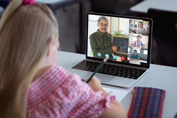 Caucasian girl with long blond hair writing notes while learning through online class on laptop