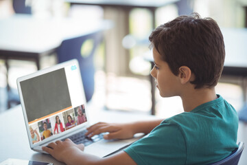Side view of caucasian boy studying online through video call on laptop while sitting at table