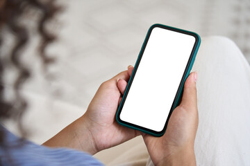 Young woman user holding smart phone mock up white empty cellphone screen in hands using mobile apps at home. Cell display mockup for advertising. Close up. Over shoulder view