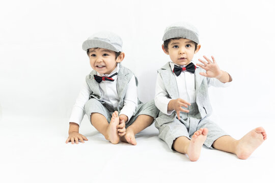 twin boys dressed in elegant dresses playing on a white background