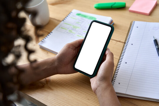 African American college girl student holding phone distance learning class using mobile tech, watching online video lesson in app studying at home school, over shoulder mock up screen view.