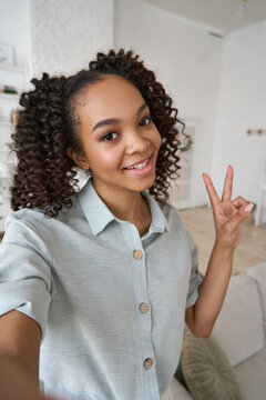 Young Happy African American Teen Girl Holding Phone Looking At Mobile Vertical Camera Streaming Vlog, Taking Selfie Portrait, Making Call Or Recording Video On Cell At Home. Cam View