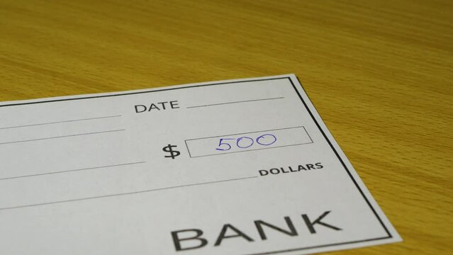 A man writes a bank check for five hundred dollars, close-up, selective focus