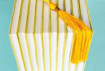 Yellow gold graduate tassel of Academic graduation hat laying on books on blue background close-up...