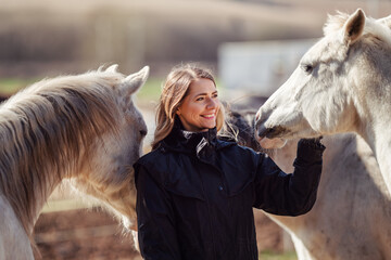 Young woman in black riding jacket standing near group of white Arabian horses smiling happy, one...
