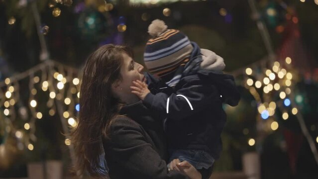 Determined little child kiss mother close Christmas tree, cold night