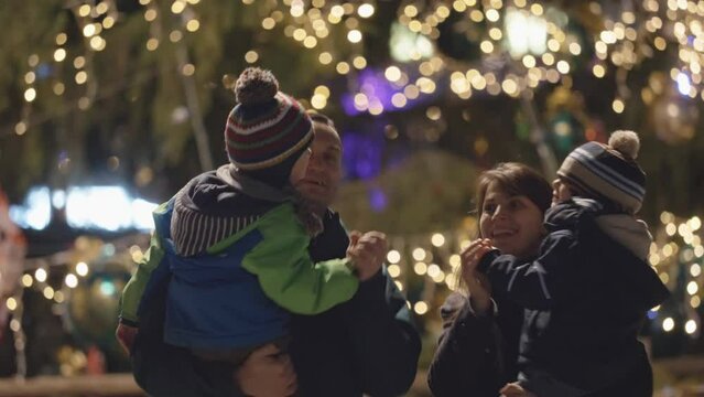 Parents dancing with little children close evening Christmas tree, brother kiss
