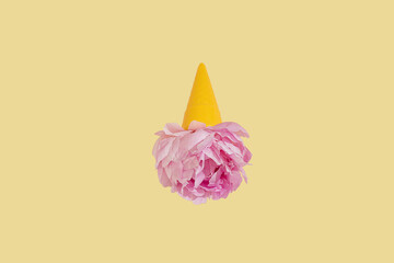 Creative yellow toy ice cream cone with pink peony fluffy flower on yellow minimal background with copy space flat lay. Botany idea for summer or spring wallpaper or greeting card. Upside down idea.
