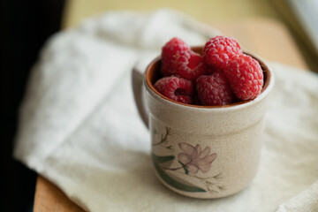 Red berries in a cup in a roustic style. Close up of fresh ruspberries in a cup on a wooden table.