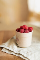 Red berries in a cup in a roustic style. Close up of fresh ruspberries in a cup on a wooden table.