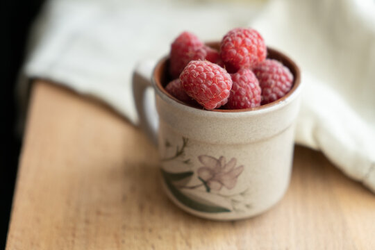 Red berries in a cup in a roustic style. Close up of fresh ruspberries in a cup on a wooden table.