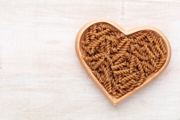 Whole grains fusilli pasta in a heart shaped wood bowl.