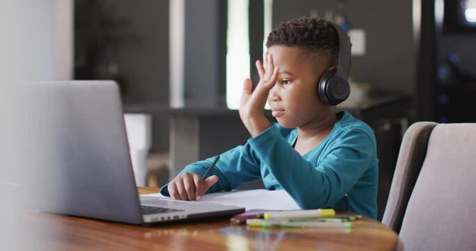Video of african american boy in headphones learning with laptop