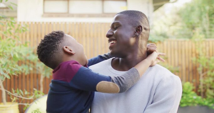 Video of happy african american father and son hugging in garden