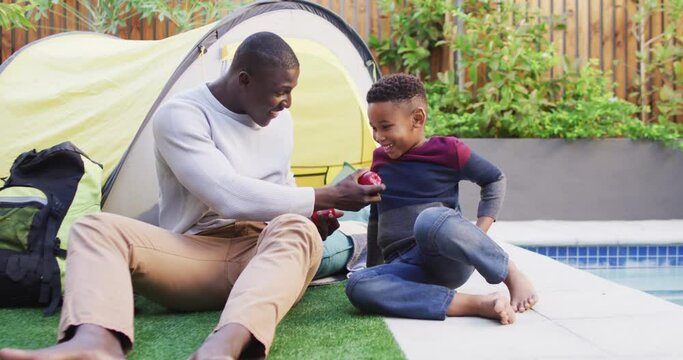 Video of happy african american father and son playing in tent in garden