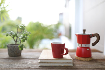Red coffee and red moka pot and notebook on brown wooden table outdoor