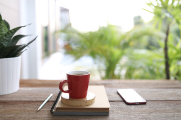 Red coffee and red phone and notebooks on brown wooden table outdoor