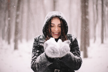 Happy smiling young woman holding snow during snowfall in winter
