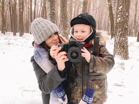Happy mother and son holding digital camera standing in park in winter