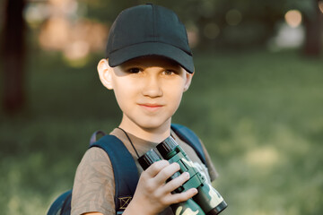 Little boy scout with backpack and binoculars during hiking in forest. Concepts of adventure, journey, scouting and hiking tourism for kids.