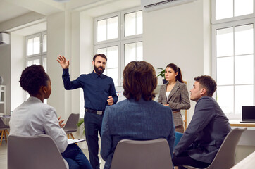 Smart male business coach or team leader talks to employees during work meeting or brainstorming....