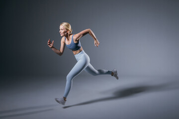 Fototapeta na wymiar Women running in studio. Female runner on blue gray background. Healthy blonde woman. Profile view of sport runner. Full length of fit girl