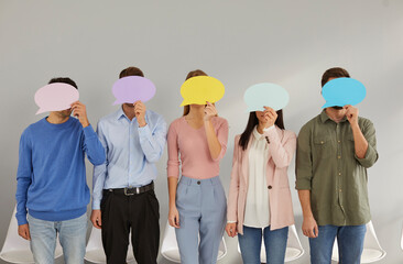 Five young people hide their faces behind empty colored speech bubbles. Various unrecognizable men...