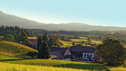 malerische Blick auf Wiesen, Berge und Bauernhof  im warmen Abendlicht in Bayern unter blauem Himmel