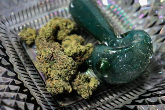 Cannabis buds on a dish next to a glass pipe
