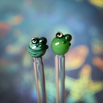 Two borosilicate glass stir sticks with tiny turtle designs on a colorful sphere