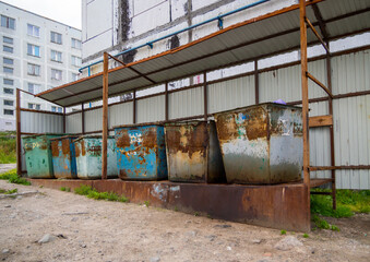 Old garbage containers stand on an equipped platform in the courtyard of the house