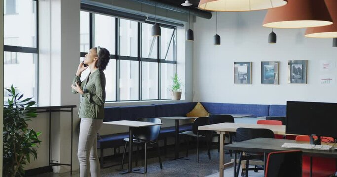 African american businesswoman at window using smartphone alone at office