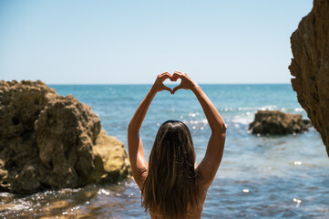 Woman in swimwear showing heart gesture at seaside