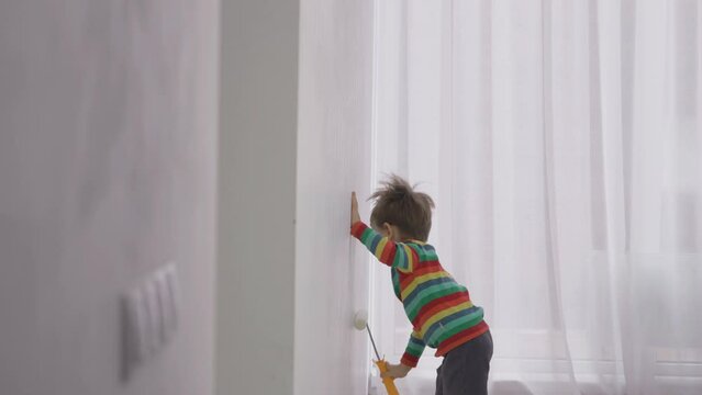 Little boy painting the entire white wall at home