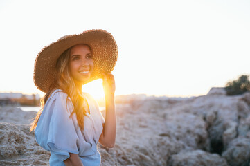 Content trendy woman smiling on rocky seashore at sunset