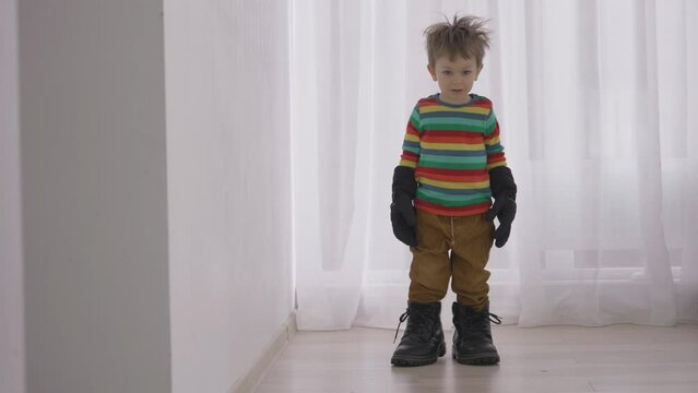 Little funny cute child wearing the big boots and gloves of his father