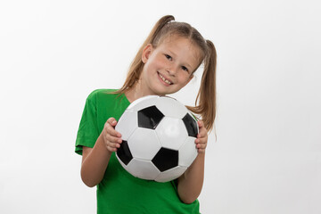 A cute girl in a green t-shirt with a soccer ball in her hand smiles isolated on a white background. A sporty caucasian kid holds the ball. Children's sports game.