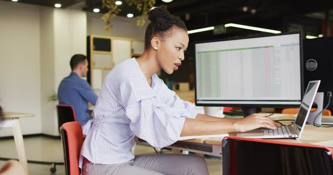 Happy african american businesswoman sitting at table and using laptop at office