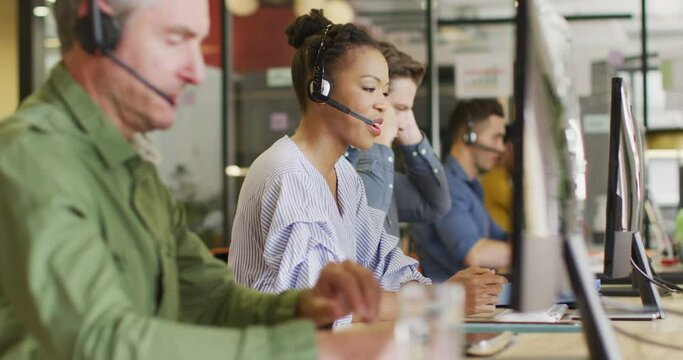 Happy diverse business people sitting at table and using phone headsets at office